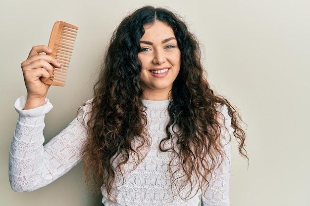 1695834948 young brunette woman with curly hair styling hair using comb looking positive happy standing smiling with confident smile showing teeth 839833 26128