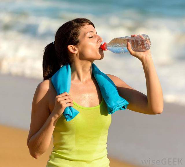 1437986409 woman in green shirt and blue towel around her neck drinking water