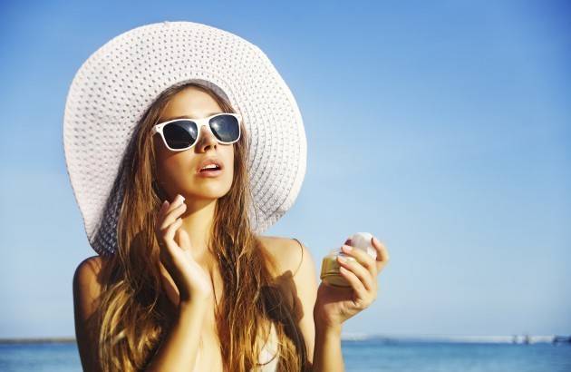 1447649846 woman in wide brimmed hat and sunglasses applying sunscreen at beach 186957862 credit istock 630x410