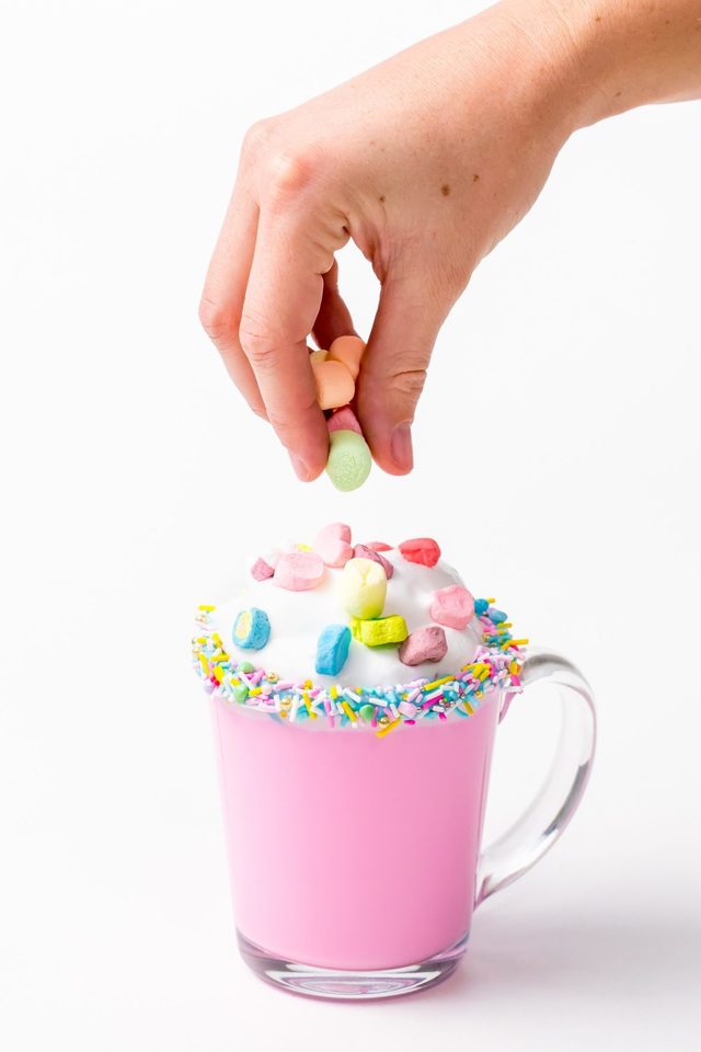 1549008095 5d4b3079 unicorn hot chocolate adding lucky charms marshmellows over the whipping cream 1200x1800